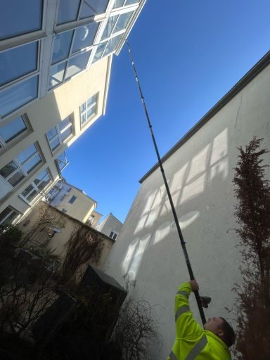 Ein Arbeiter mit einer langen Stange reinigt ein Fenster an einem hohen Gebäude.