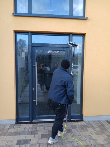 Ein Mann reinigt eine Glastür mit einem Wischmop vor einem modernen Gebäude.
