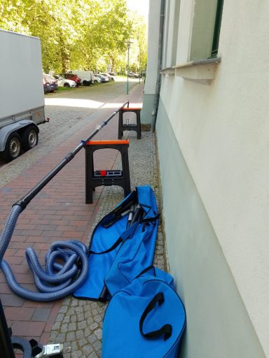 Schwarzer Tisch, blaue Schläuche und Ausrüstung auf einem Gehweg neben Wohngebäuden.
