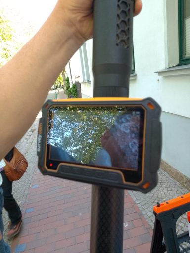 Schwarzer Handheld-Bildschirm mit orangefarbenem Rand, montiert auf einem Stangenhalter.