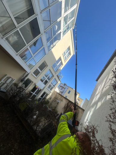Arbeiter mit einer langen Stange zur Reinigung eines Fensters an einem Hochhaus.