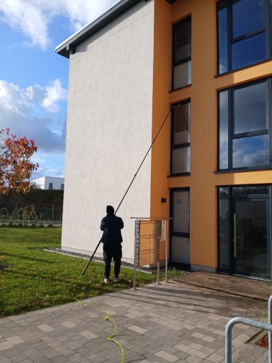 Person mit Leiter neben einem modernen, zweifarbigen Gebäude im Freien.