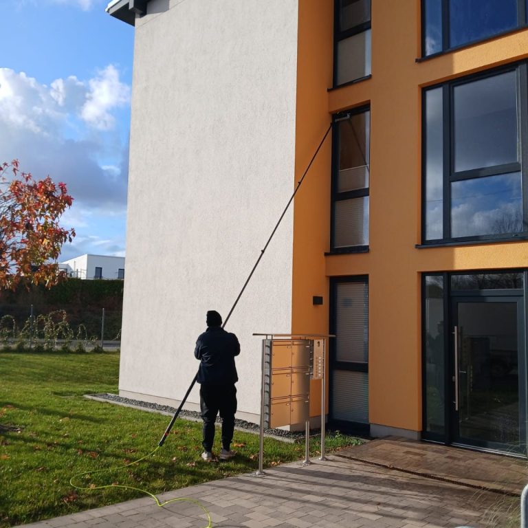 Eine Person reinigt die Fassade eines modernen Gebäudes mit einer langen Stange.