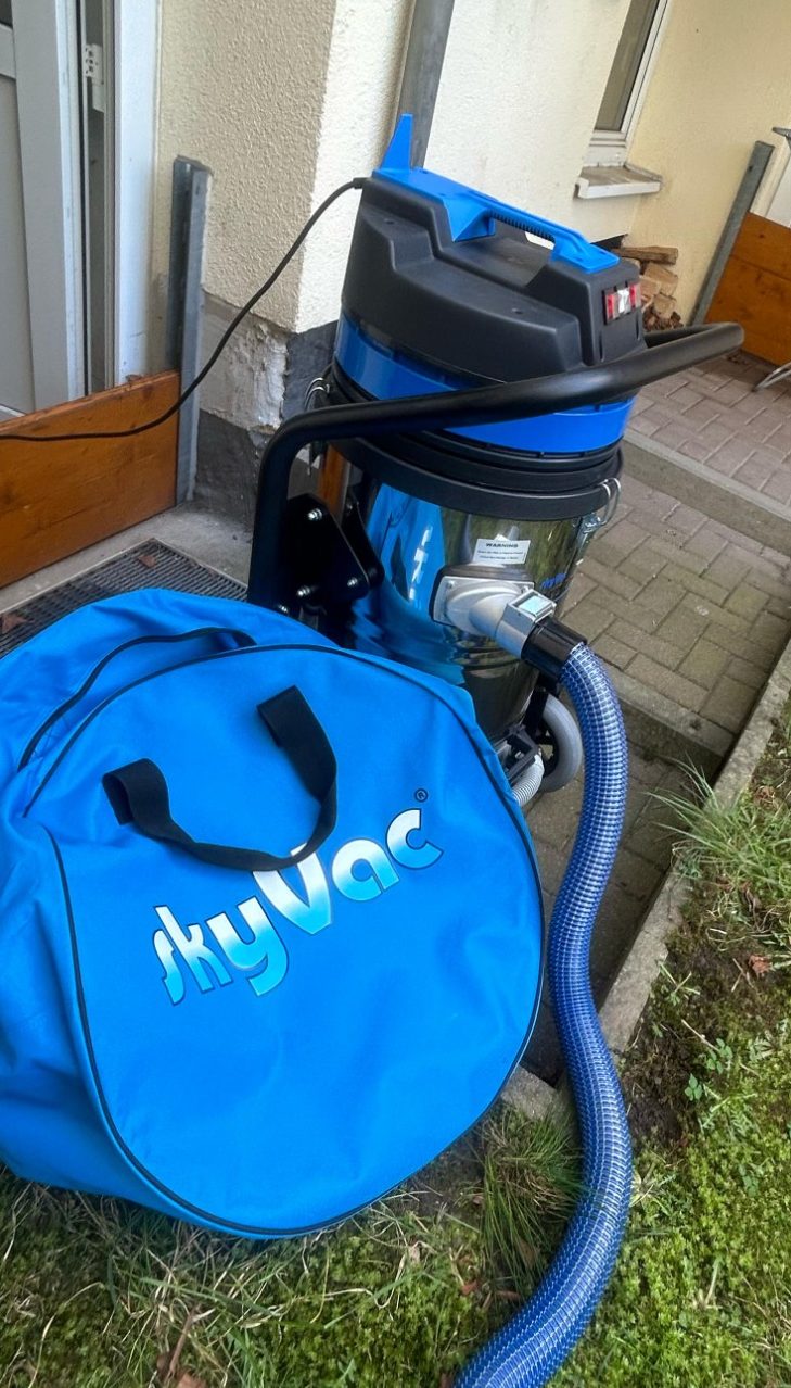 SkyVac Profi-Set zur Dachrinnenreinigung 12 Meter Blauer Staubsauger mit Schlauch und Tasche, auf einem Gehweg vor einer Tür.