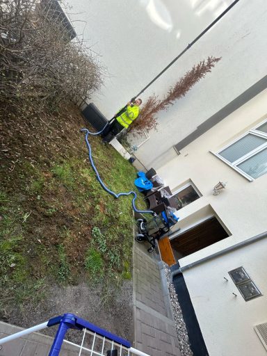 Ein Arbeiter mit Warnweste steht neben einem blauen Gerät in einem Garten.